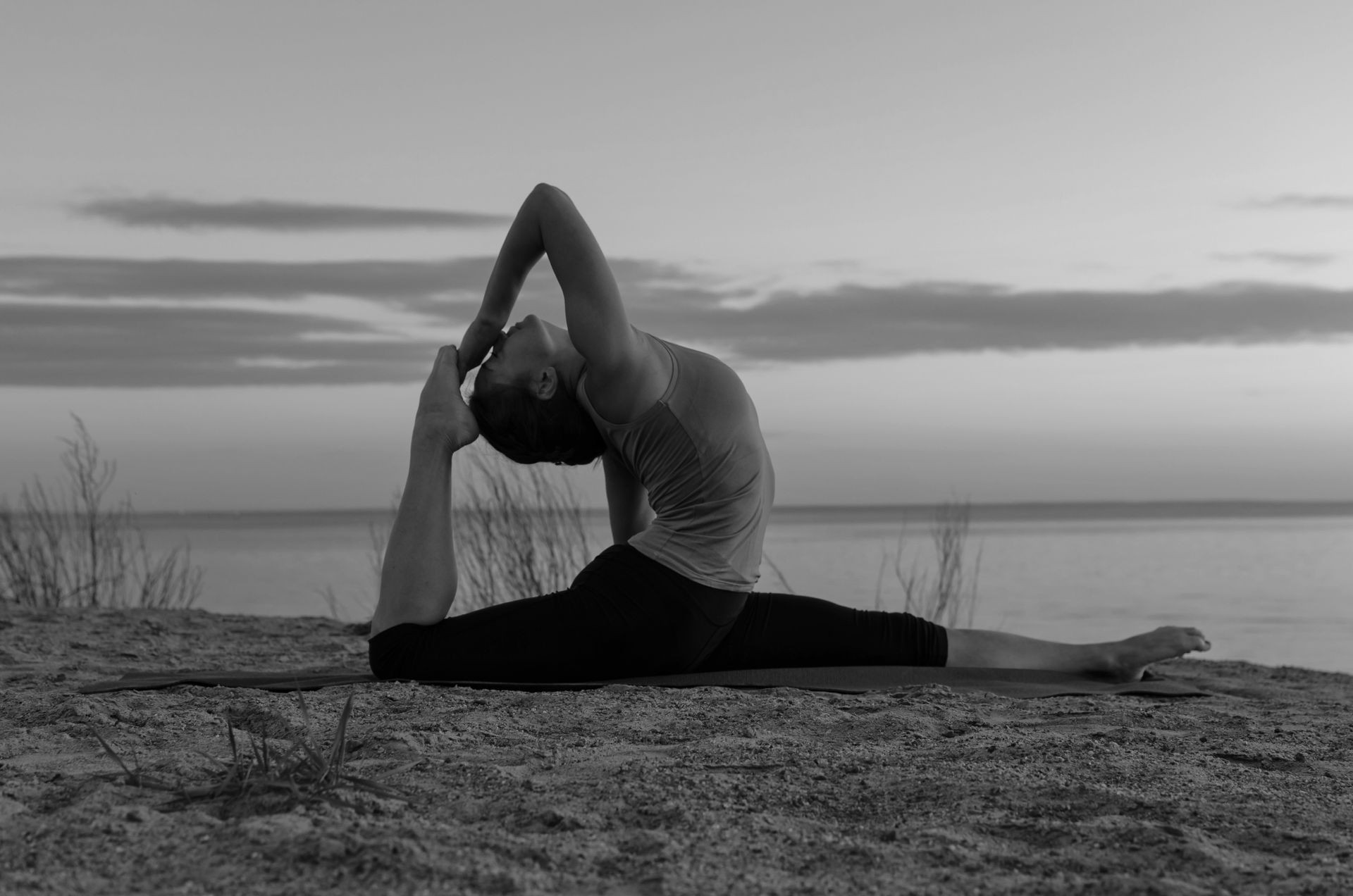Silhouette of woman with sea and sunset background making yoga exercises, asanas on the beach. Black and white picture.