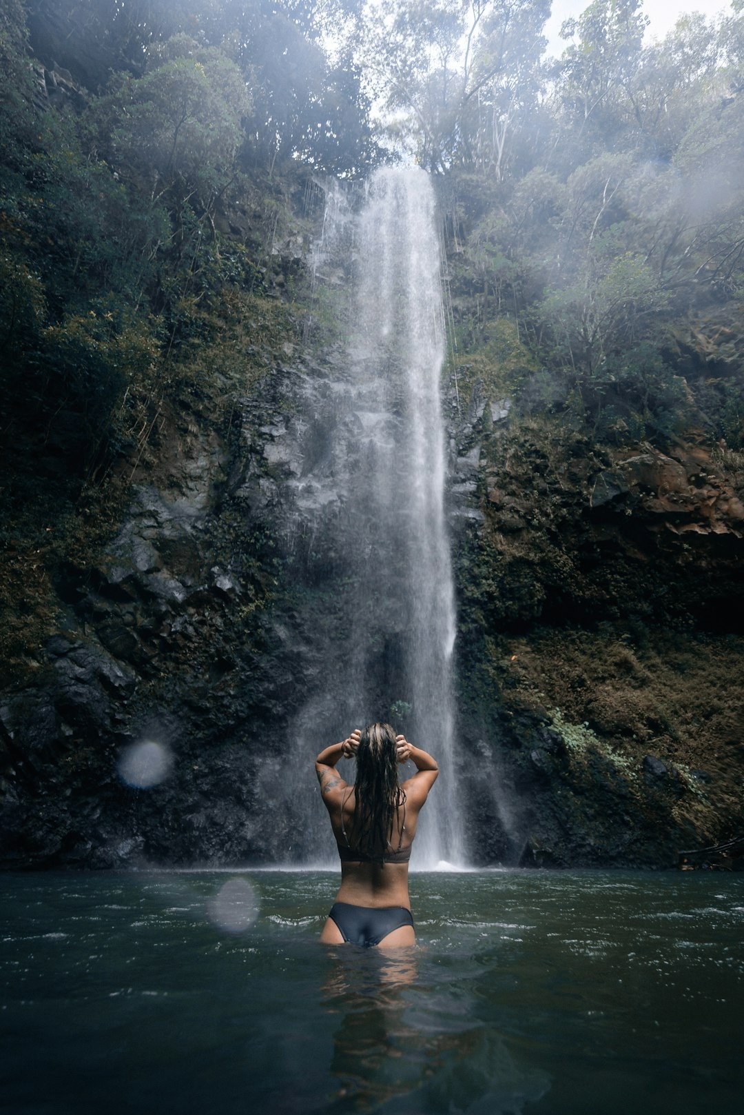 a woman standing in the water in front of a waterfall